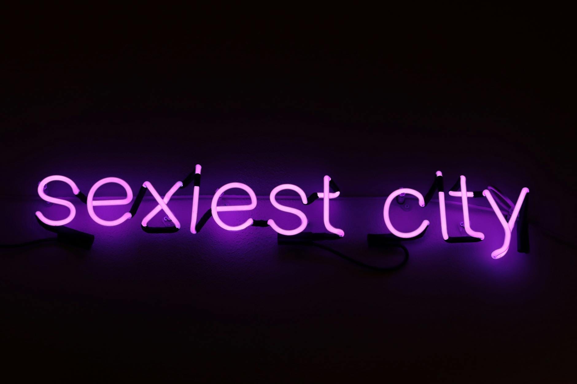 Imprezy LGBT+ w Atenach: dzielnice, bary i jak poruszać się nocą po mieście Neonowy fioletowy napis sexiest city nocą w Atenach