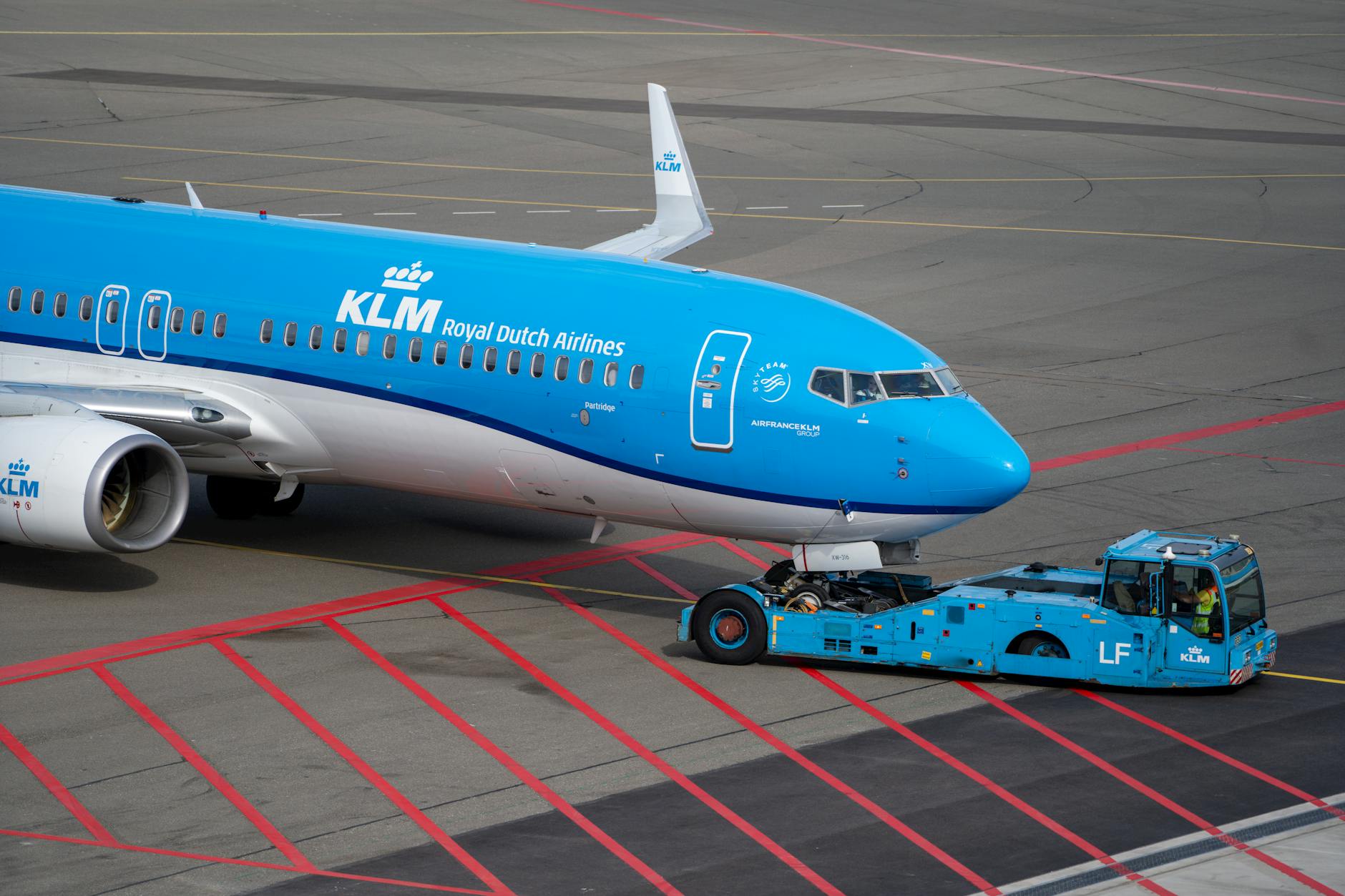 Samolot KLM holowany po płycie lotniska przez niebieski pojazd