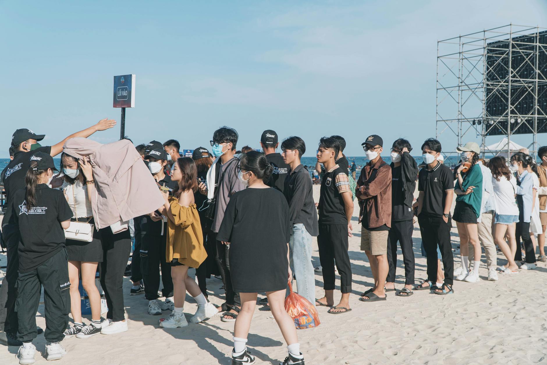 Ludzie w maseczkach stojący w kolejce przy wejściu na imprezę plenerową