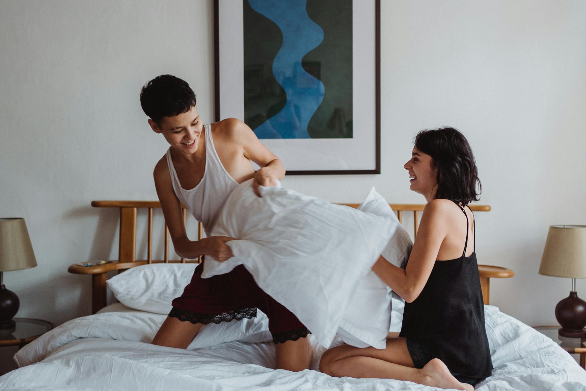 Uśmiechnięta para gejów na bitwie na poduszki w przytulnej sypialni