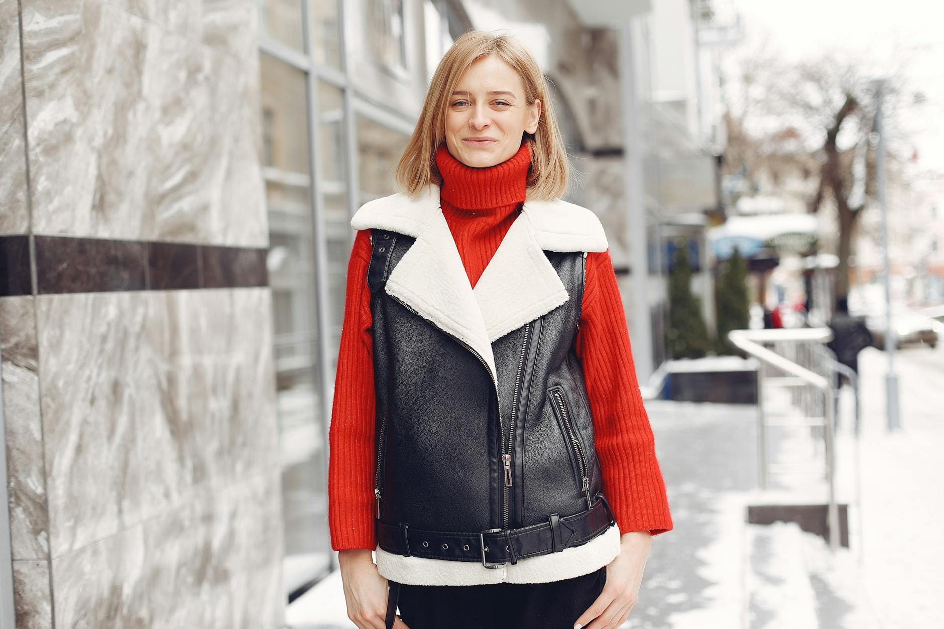 Blondynka w zimowym płaszczu pozuje pewnie na ośnieżonej ulicy miasta