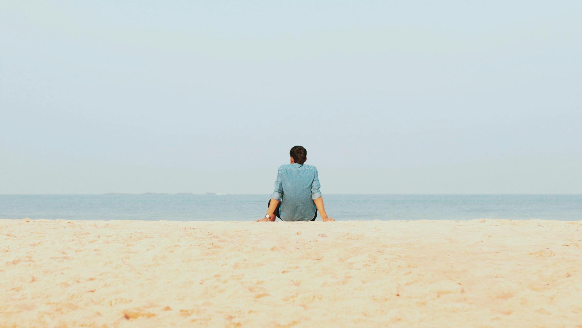 Mężczyzna siedzi samotnie na piaszczystej plaży na Cyprze, patrząc na morze