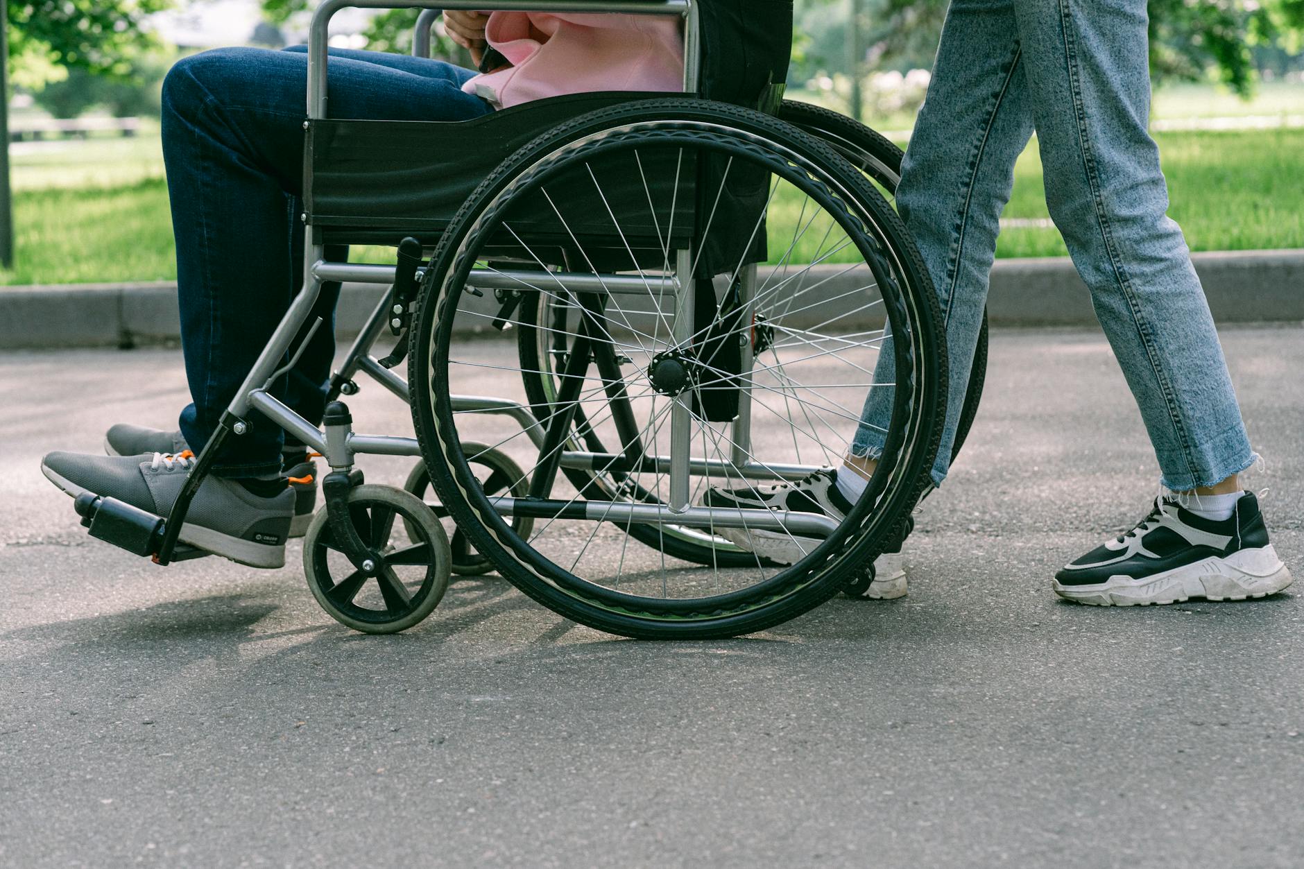 Osoba na wózku inwalidzkim z asystentem na słonecznym chodniku