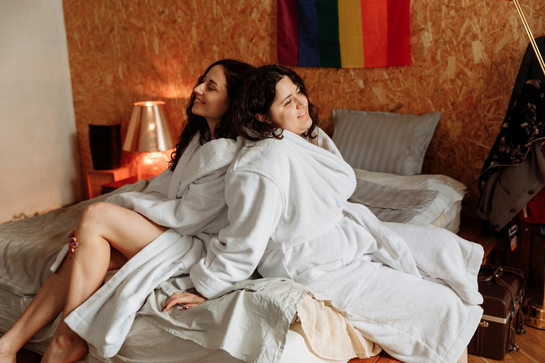 Para LGBT+ w szlafrokach odpoczywa w sypialni z tęczową flagą