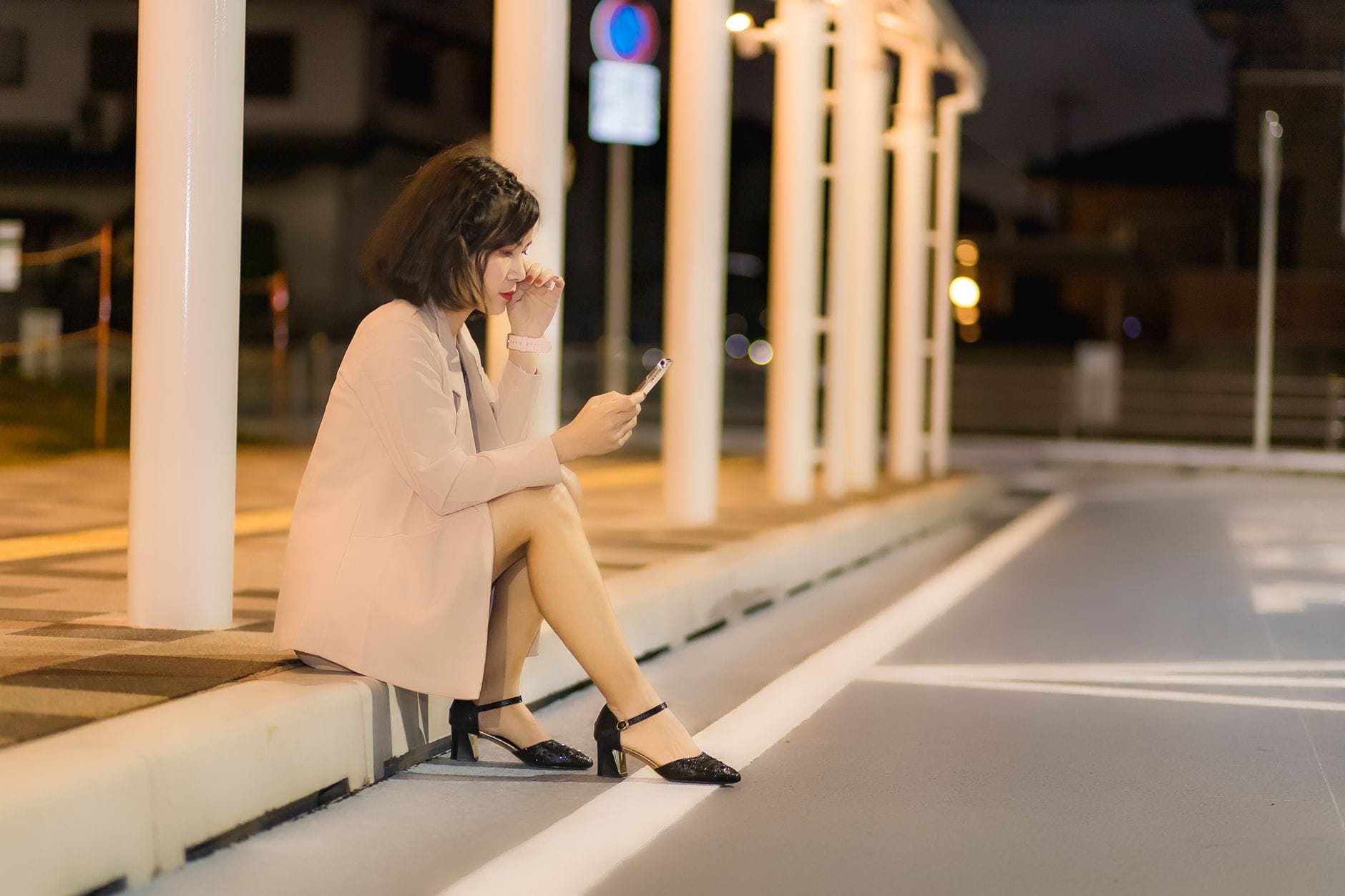 Kobieta samotnie siedzi nocą na chodniku i zamawia transport w telefonie