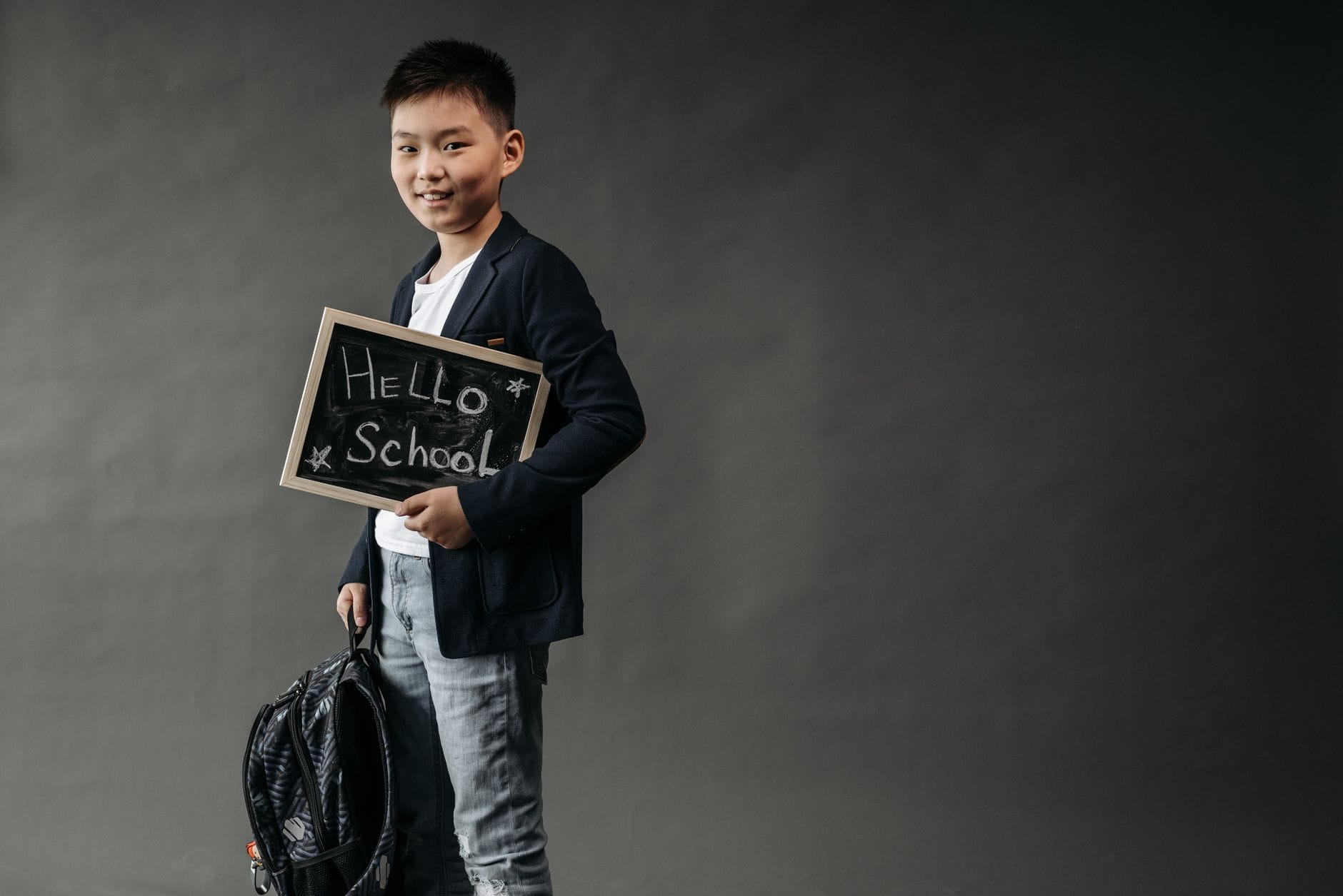 Chłopiec z plecakiem trzyma tabliczkę z napisem Hello School