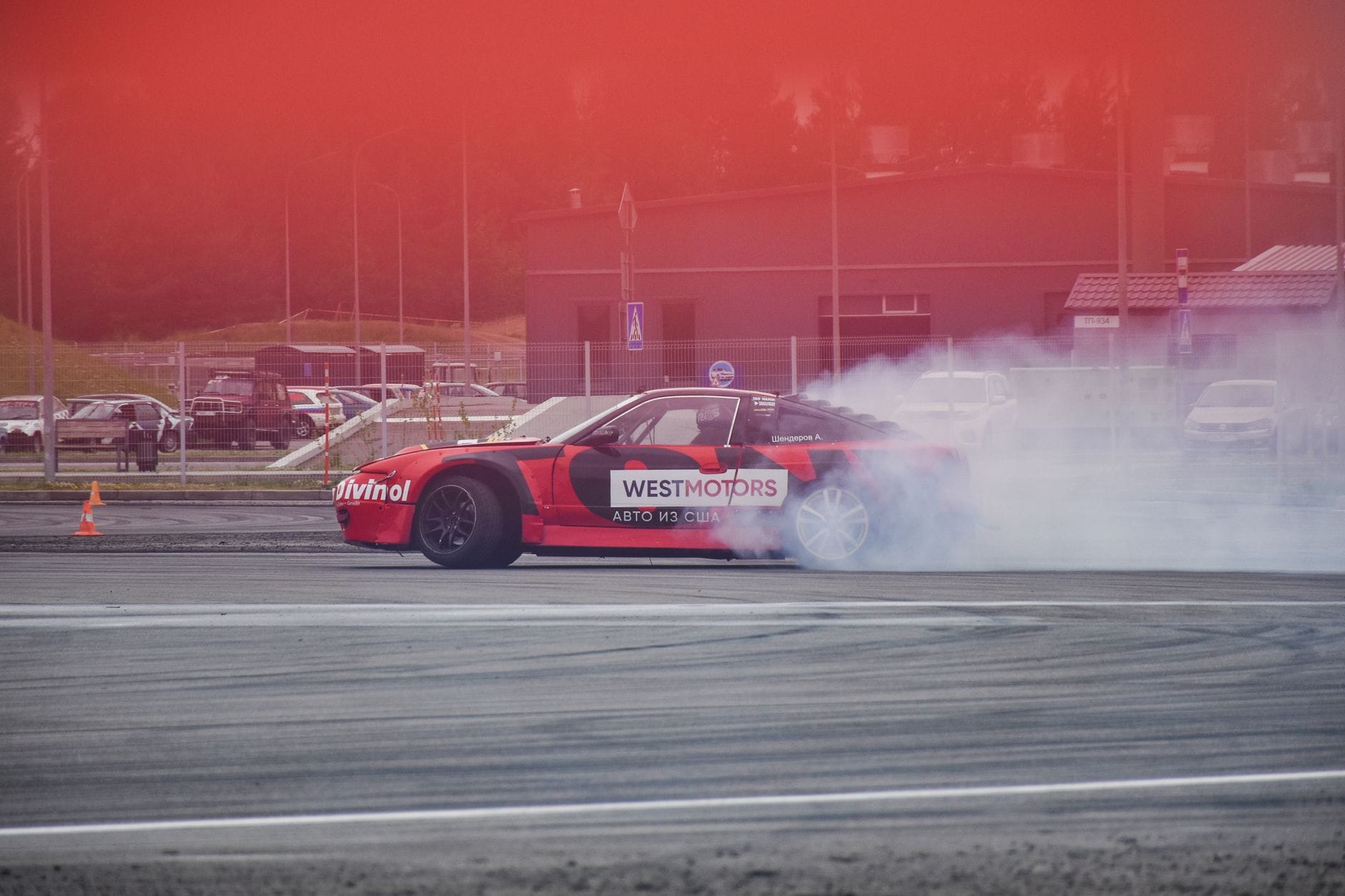 Czerwone BMW w kontrolowanym drifcie na torze, z kłębem dymu