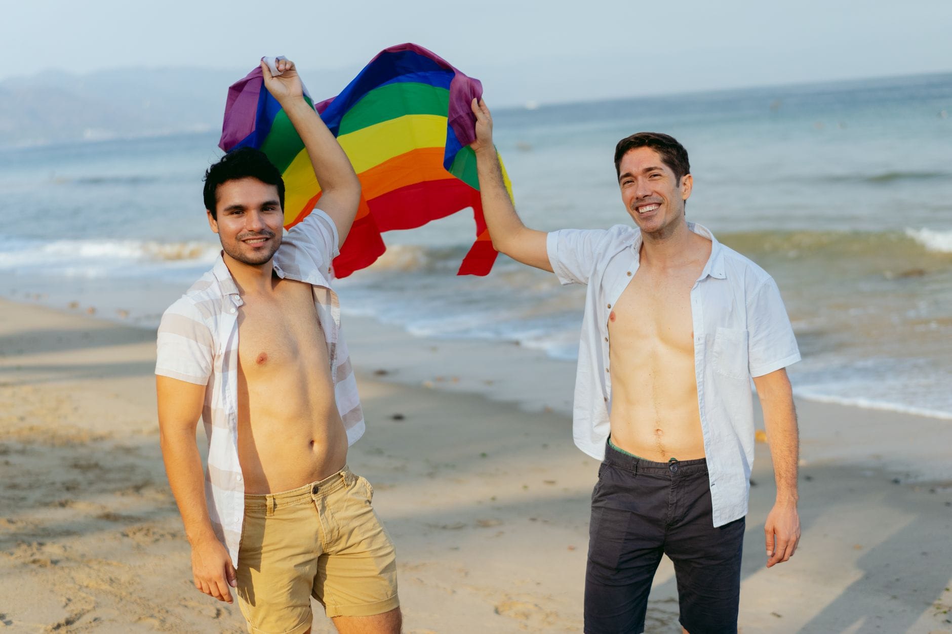 Dwóch mężczyzn z tęczową flagą świętujących na słonecznej plaży