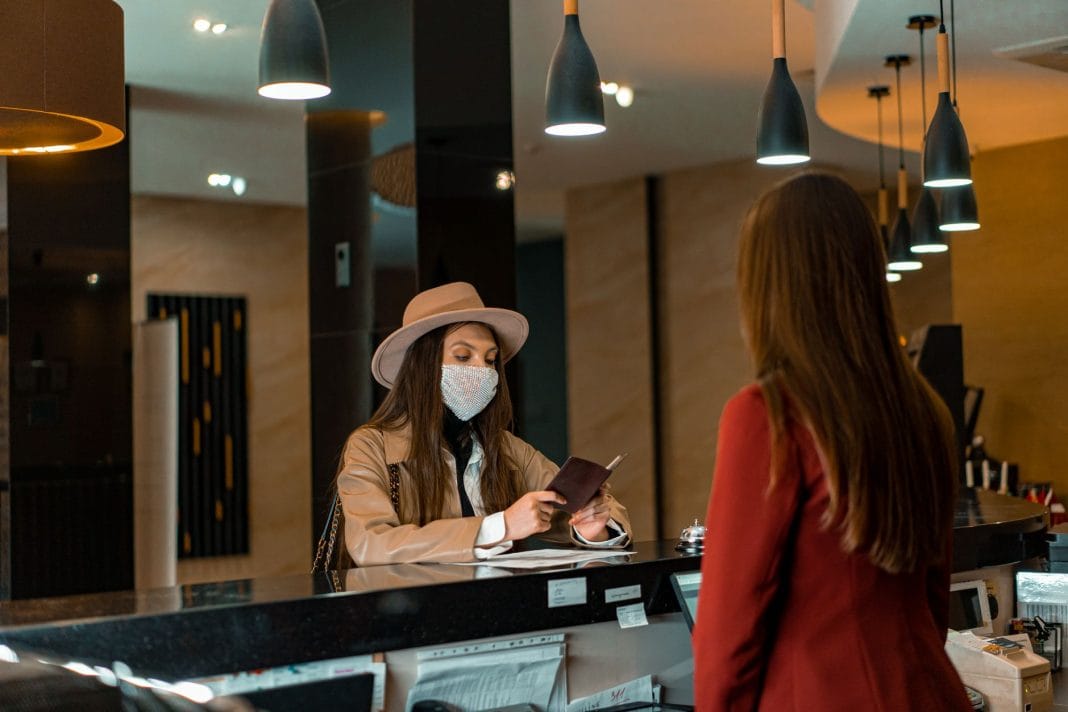Kobieta w maseczce melduje się w recepcji hotelu